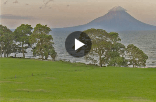 Thumbnail of green grass sloping down to large lake with mountain in distance