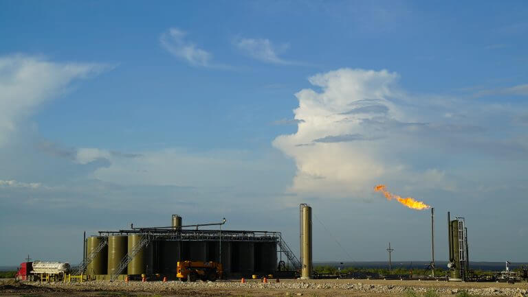 Oil and gas well in Permian Base. Blue sky with lit flare and tanker trucks present