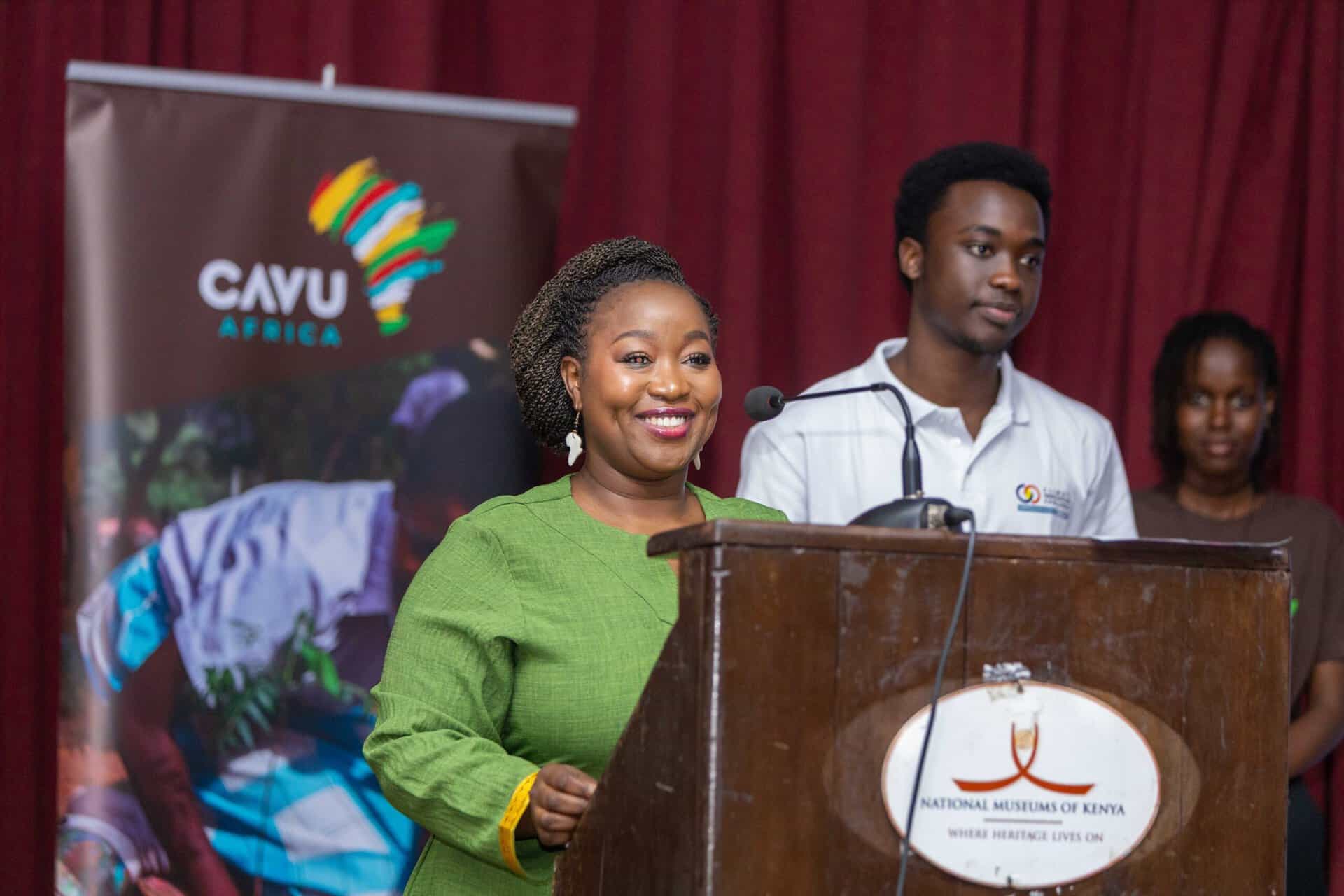 A woman in a green outfit speaks at a podium with a National Museums of Kenya sign, while two people stand behind her and a CAYU Africa banner appears in the background for the Hope in Action Newsletter, July 2026 edition.