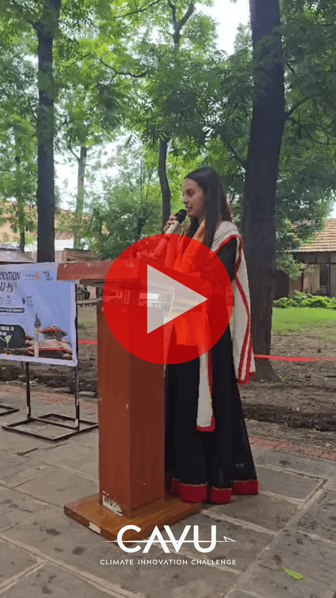 At an outdoor podium during the July 2026 event for climate innovation, a woman in a black and white sari addresses attendees, with trees and banners providing a vibrant backdrop—an inspiring moment later featured in the Hope in Action Newsletter.